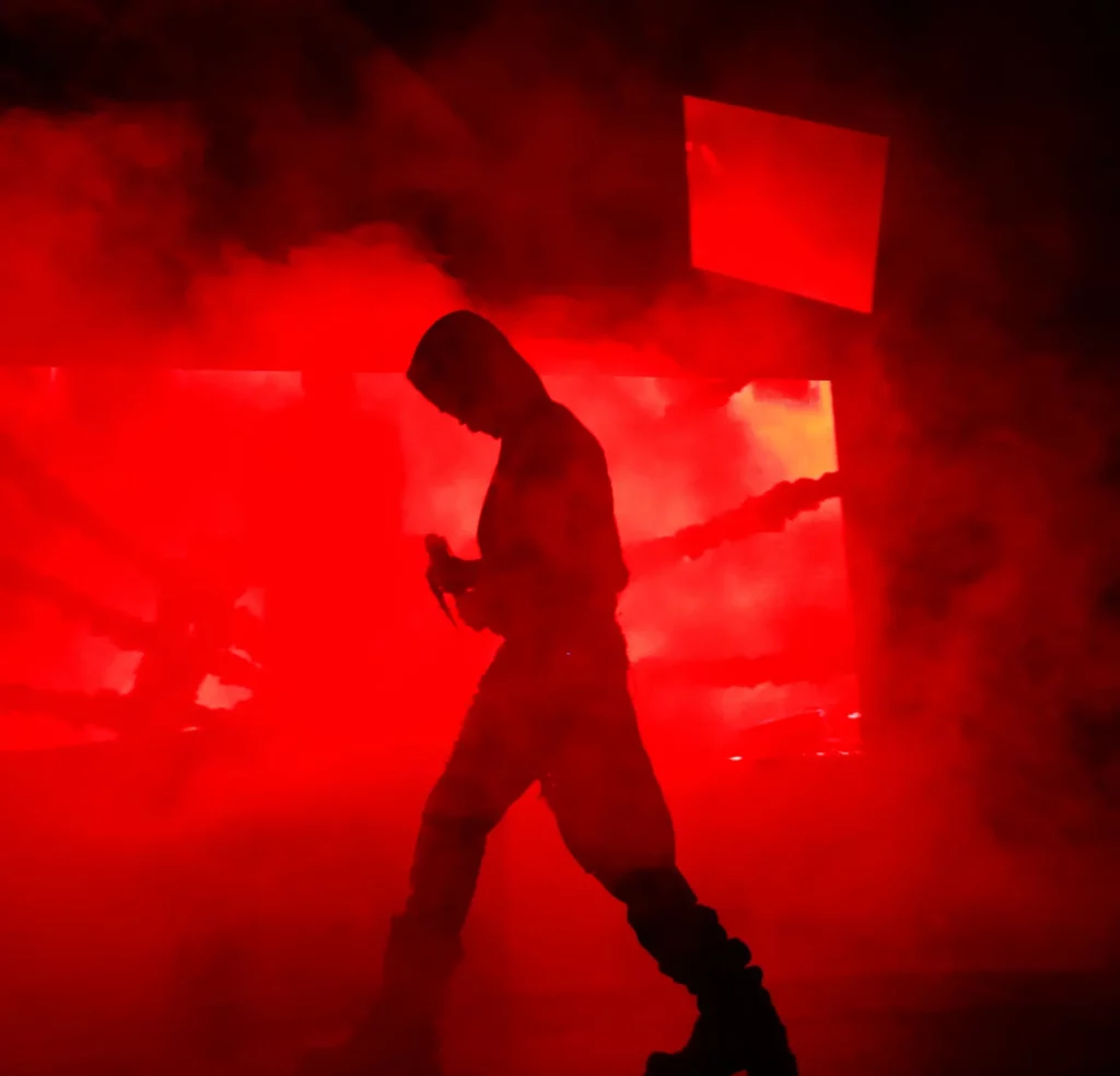 Silhouette d’un artiste marchant sur scène dans une lumière rouge intense et entouré de fumée.