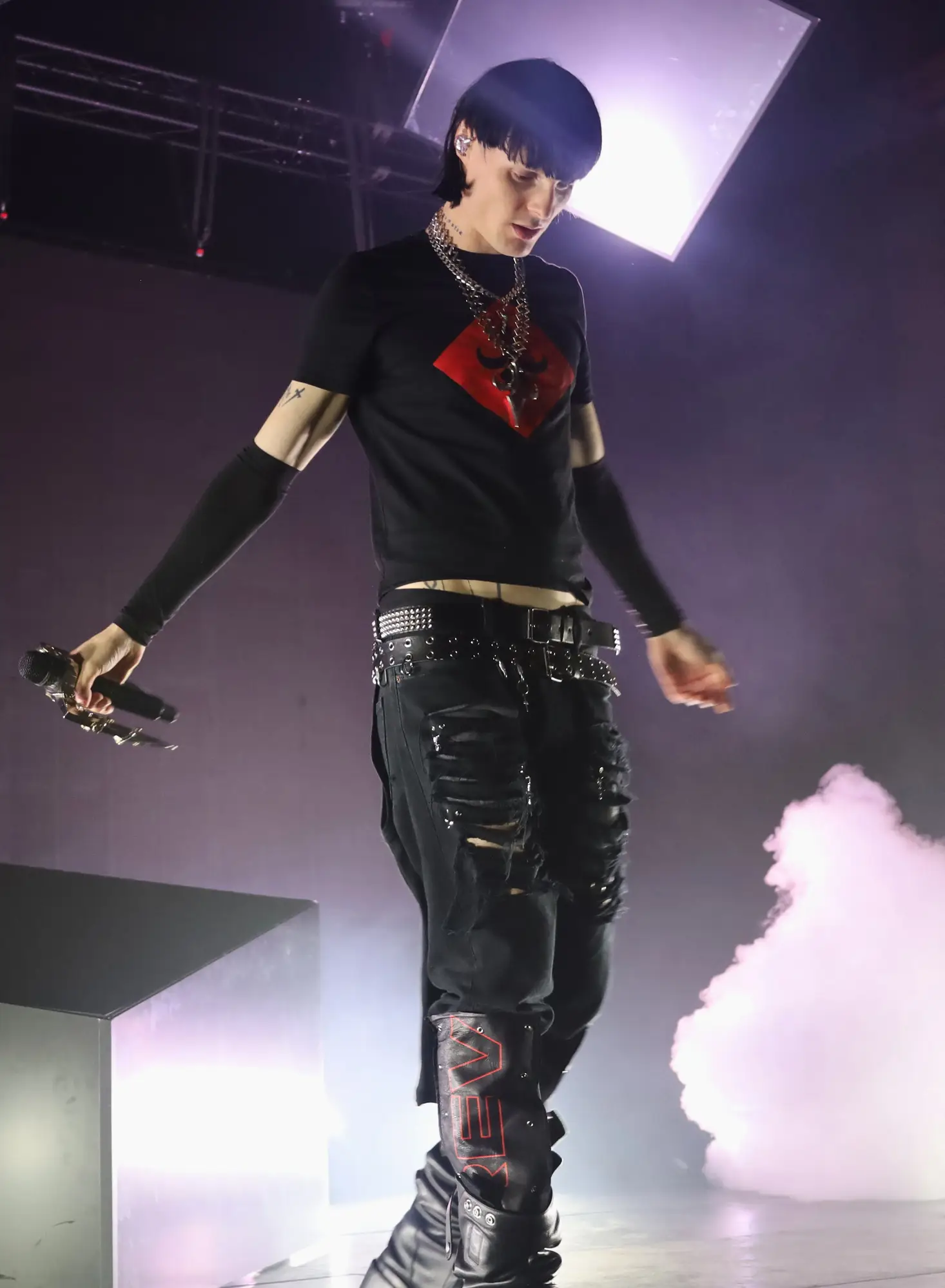 Artiste sur scène tenant un micro, éclairé par une lumière blanche avec de la fumée derrière lui.