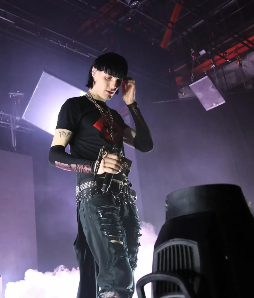 Artiste sur scène tenant un micro, éclairé par des projecteurs avec de la fumée en arrière-plan.