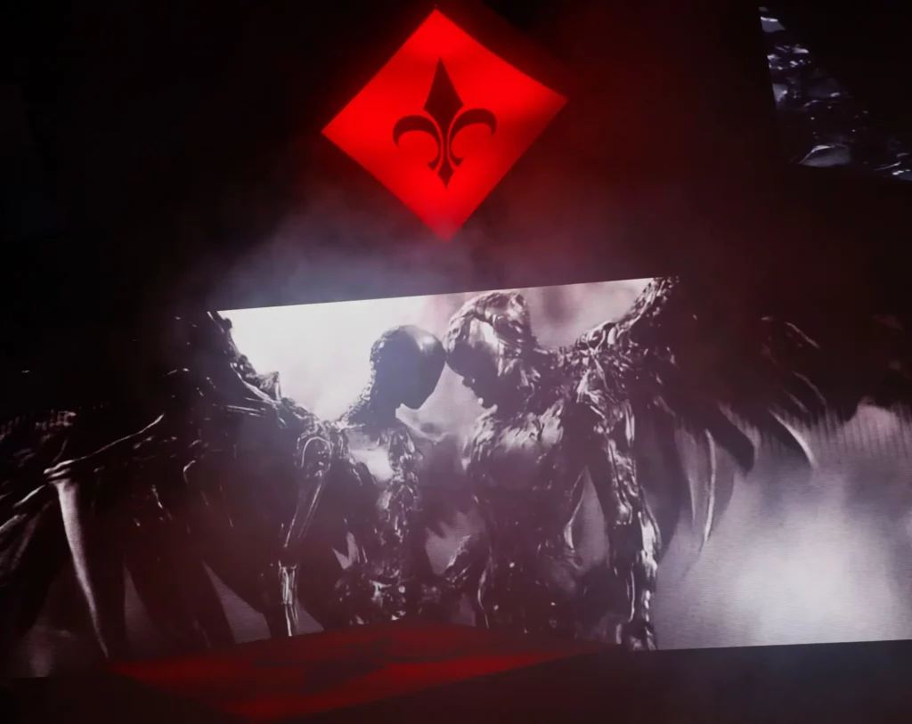 Visuel de deux créatures ailées en noir et blanc projeté sur un écran de scène, sous un symbole rouge illuminé.