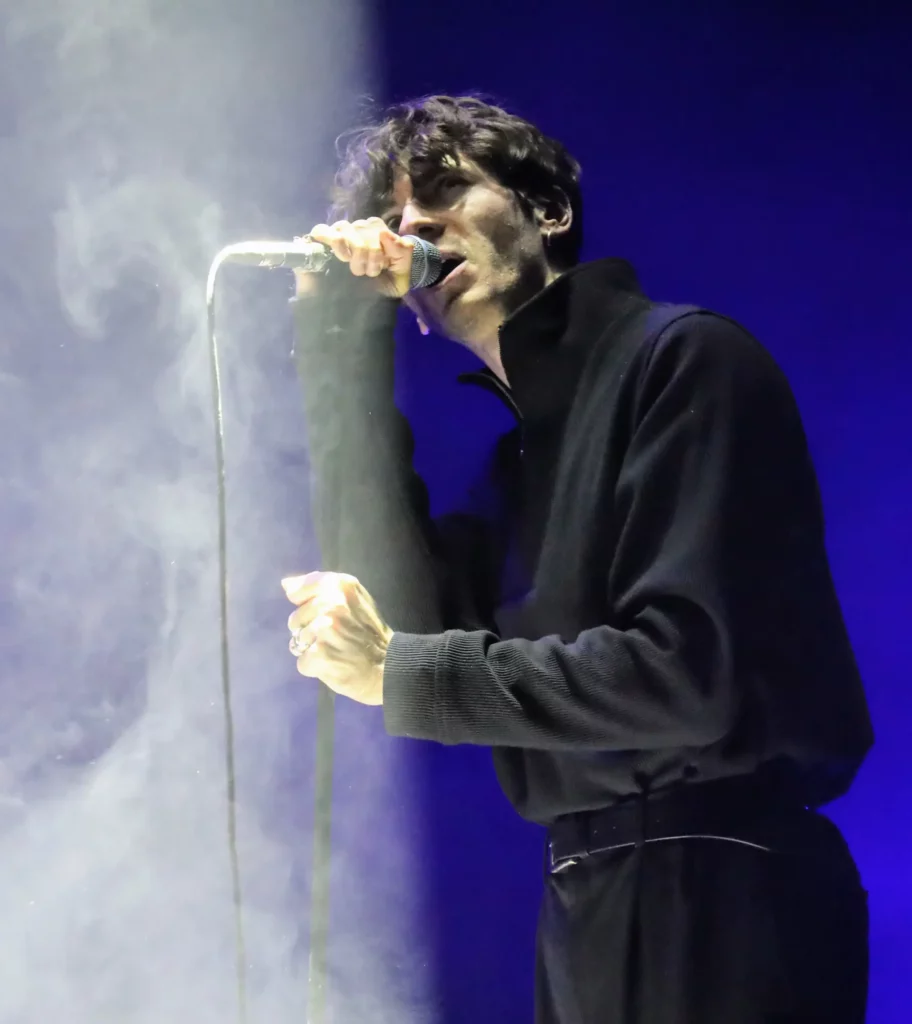 Chanteur tenant un micro sur scène, baigné dans une lumière bleue et de la fumée.