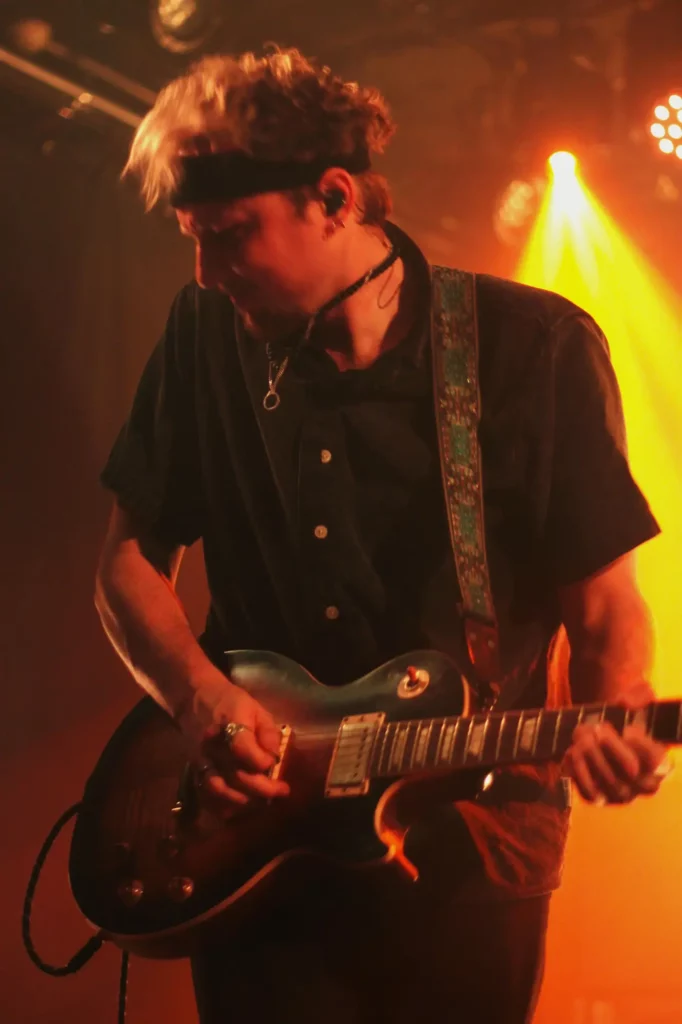 Guitariste jouant sur scène sous un éclairage orange intense.