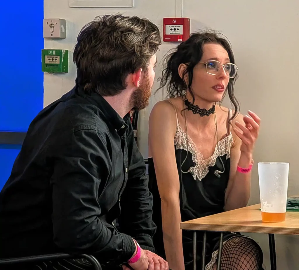 Deux personnes discutant assises à une table, avec un gobelet à moitié rempli au premier plan.