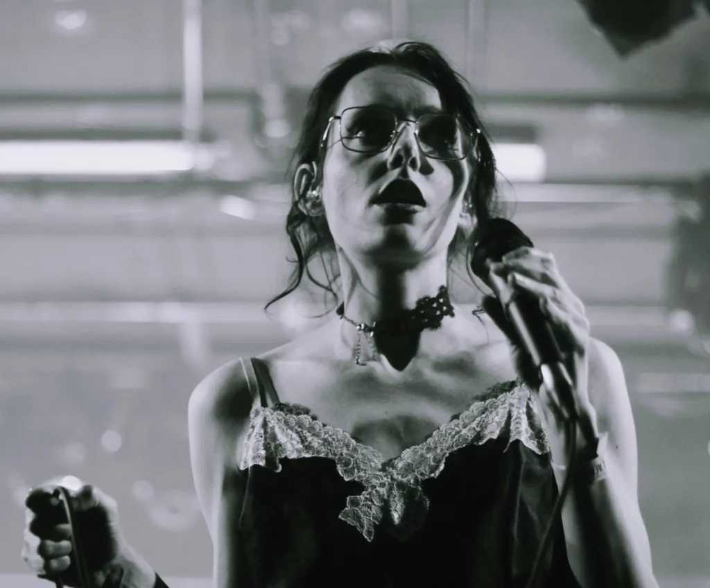 Chanteuse tenant un micro sur scène, captée en noir et blanc sous un éclairage tamisé.