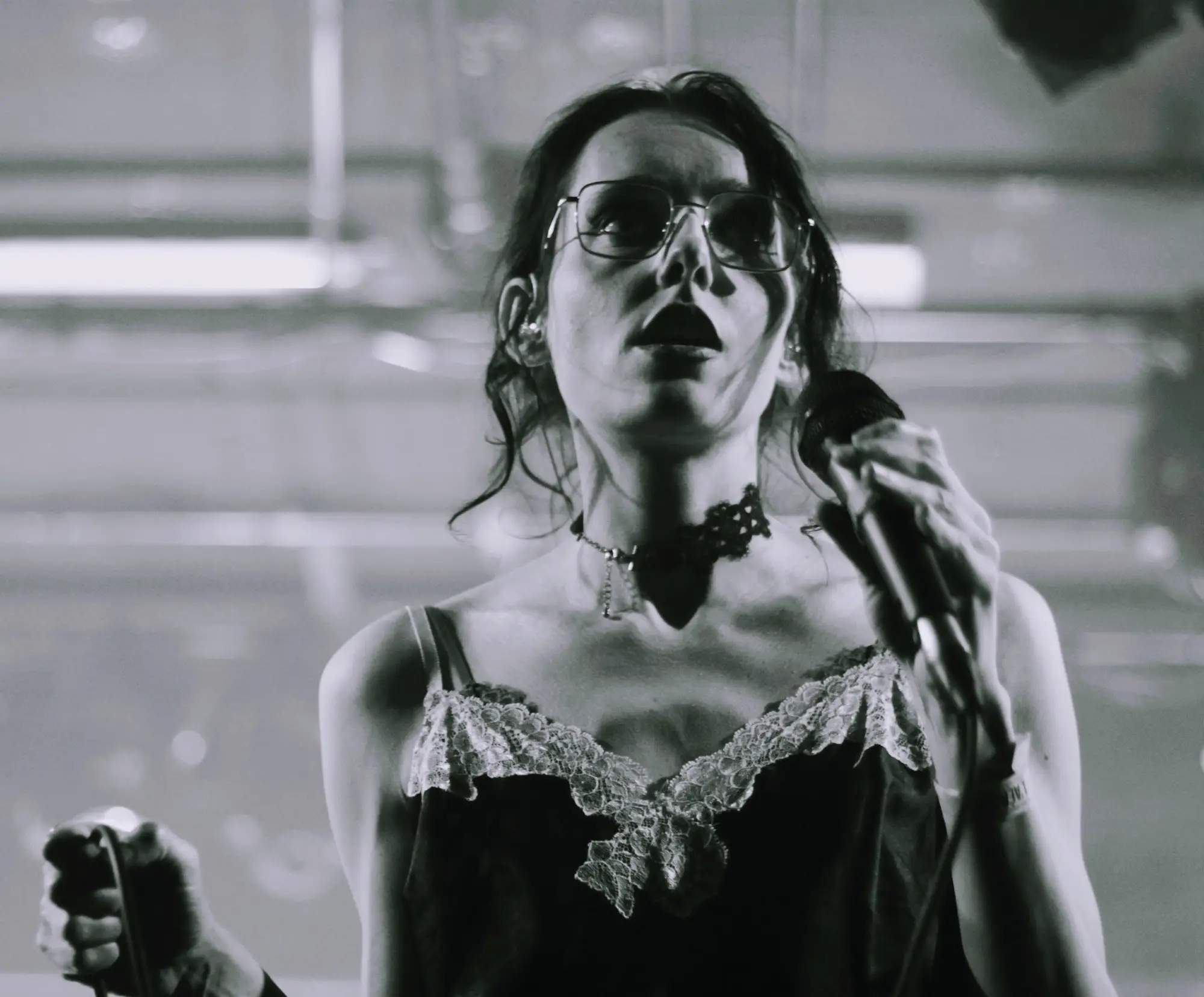 Chanteuse tenant un micro sur scène, captée en noir et blanc sous un éclairage tamisé.