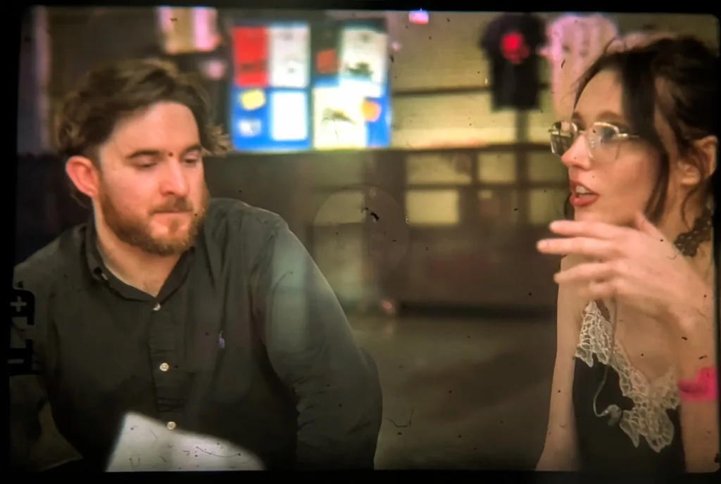 Deux personnes discutant dans un espace intérieur, vue légèrement floue comme à travers une vitre.