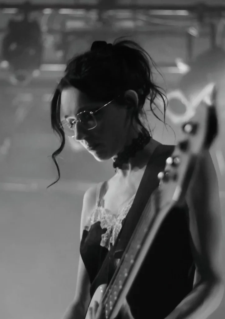 Bassiste jouant sur scène, captée en noir et blanc sous un éclairage doux.