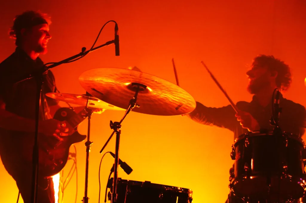 Guitariste et batteur jouant ensemble sur scène dans un éclairage orange intense.
