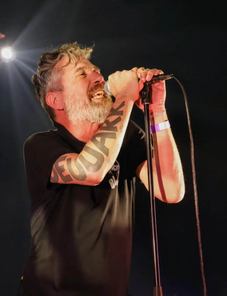 Le chanteur des Fatals Picards sur scène lors d’un concert éclairé par un spot lumineux blanc.