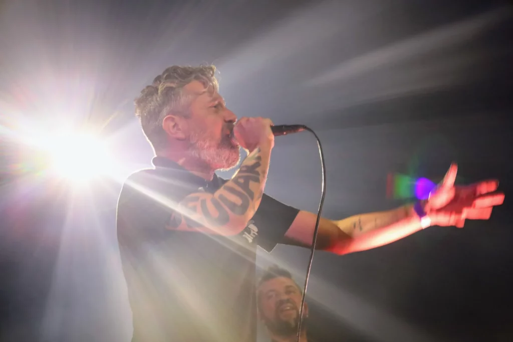 Le chanteur des Fatals Picards en concert, éclairé par les projecteurs sur scène.