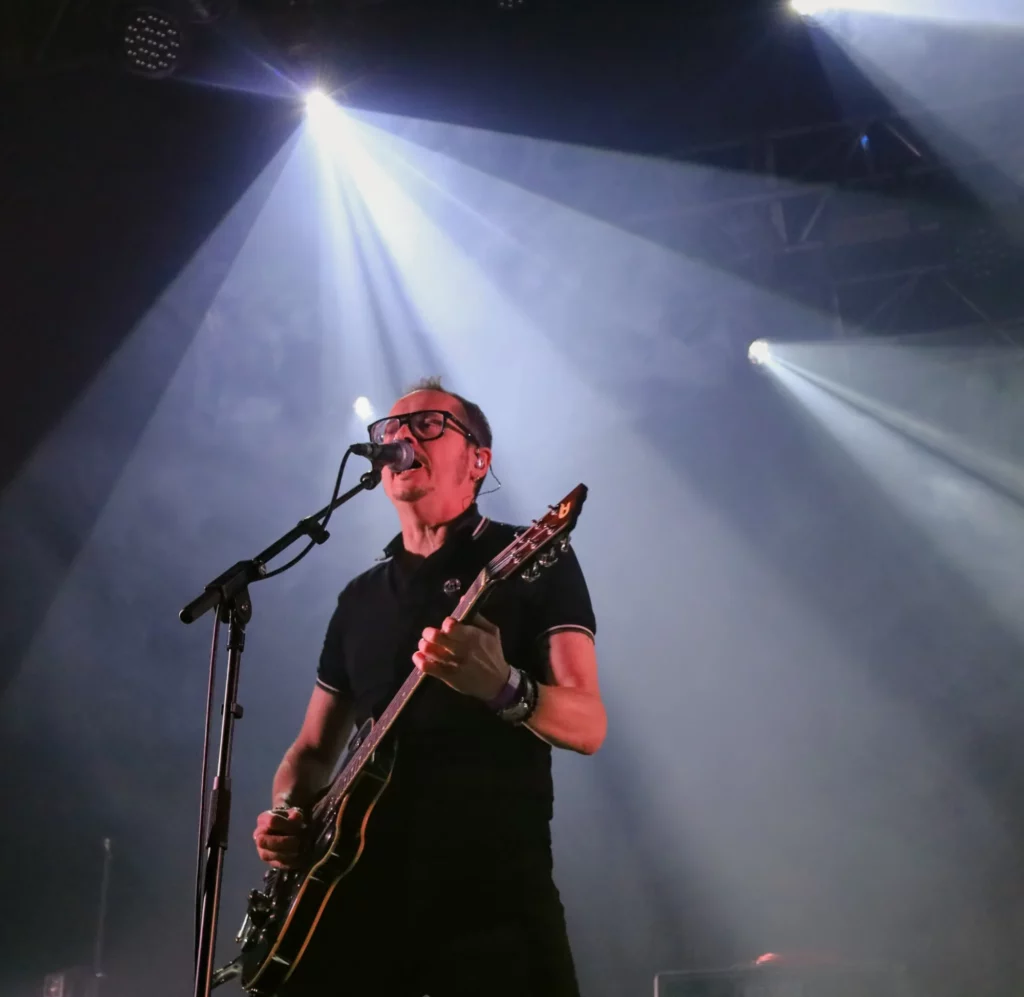 Chanteur et guitariste des Fatal Picards sur scène interprétant un titre et éclairé par des lumières blanches