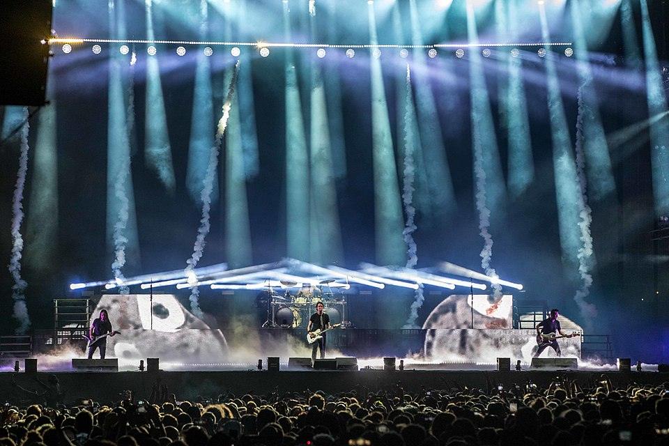 Groupe gojira sur scène au Helfest avec des lumières bleus en fond et un public devant la scène