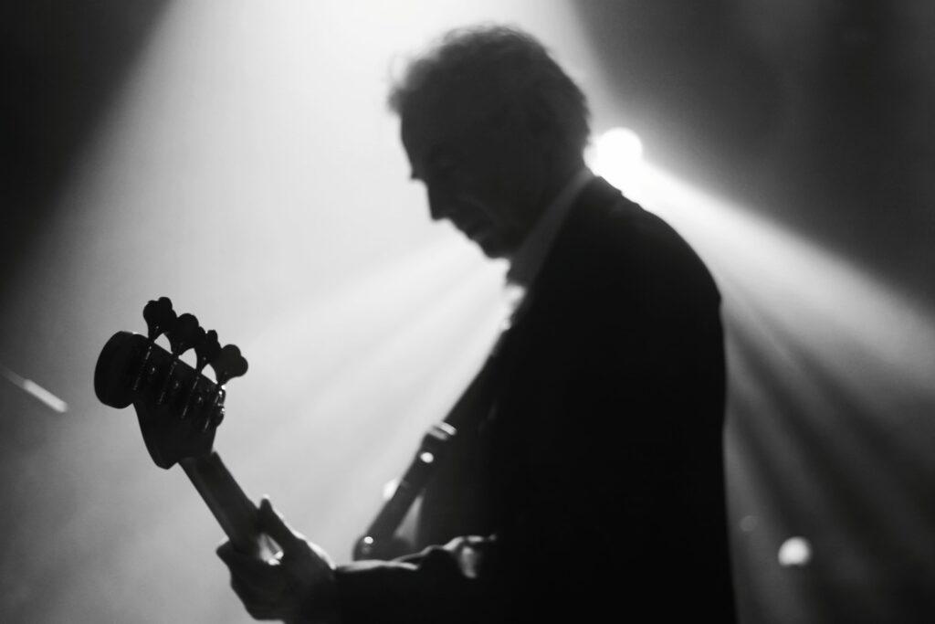 Bassiste silhouette profil costume sombre chemise blanche basse Jazz sunburst éclairage spotlight oranger scène concert fumée