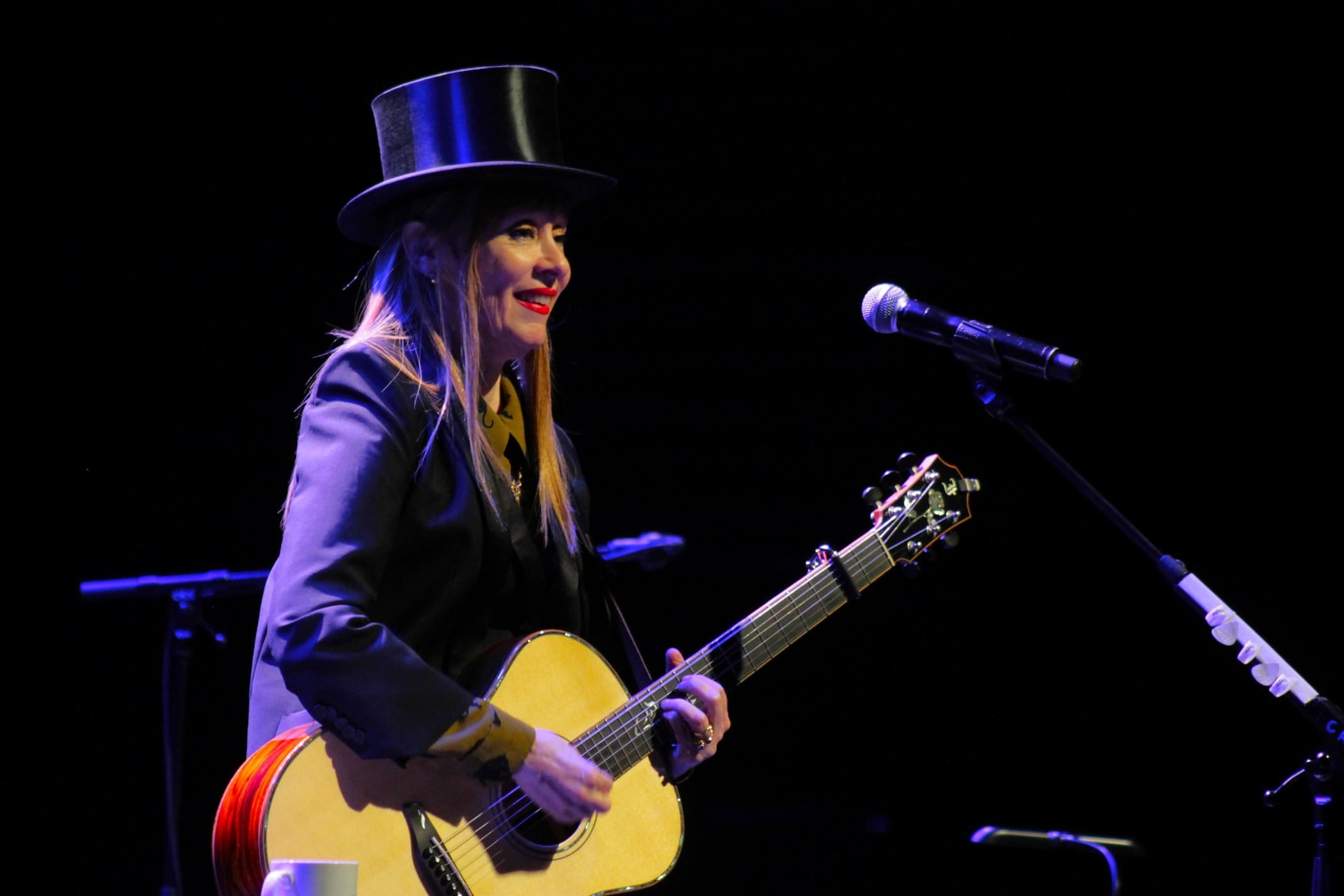 Guitariste femme chapeau haut de forme cheveux longs guitare acoustique beige scène concert sombre lèvres rouges