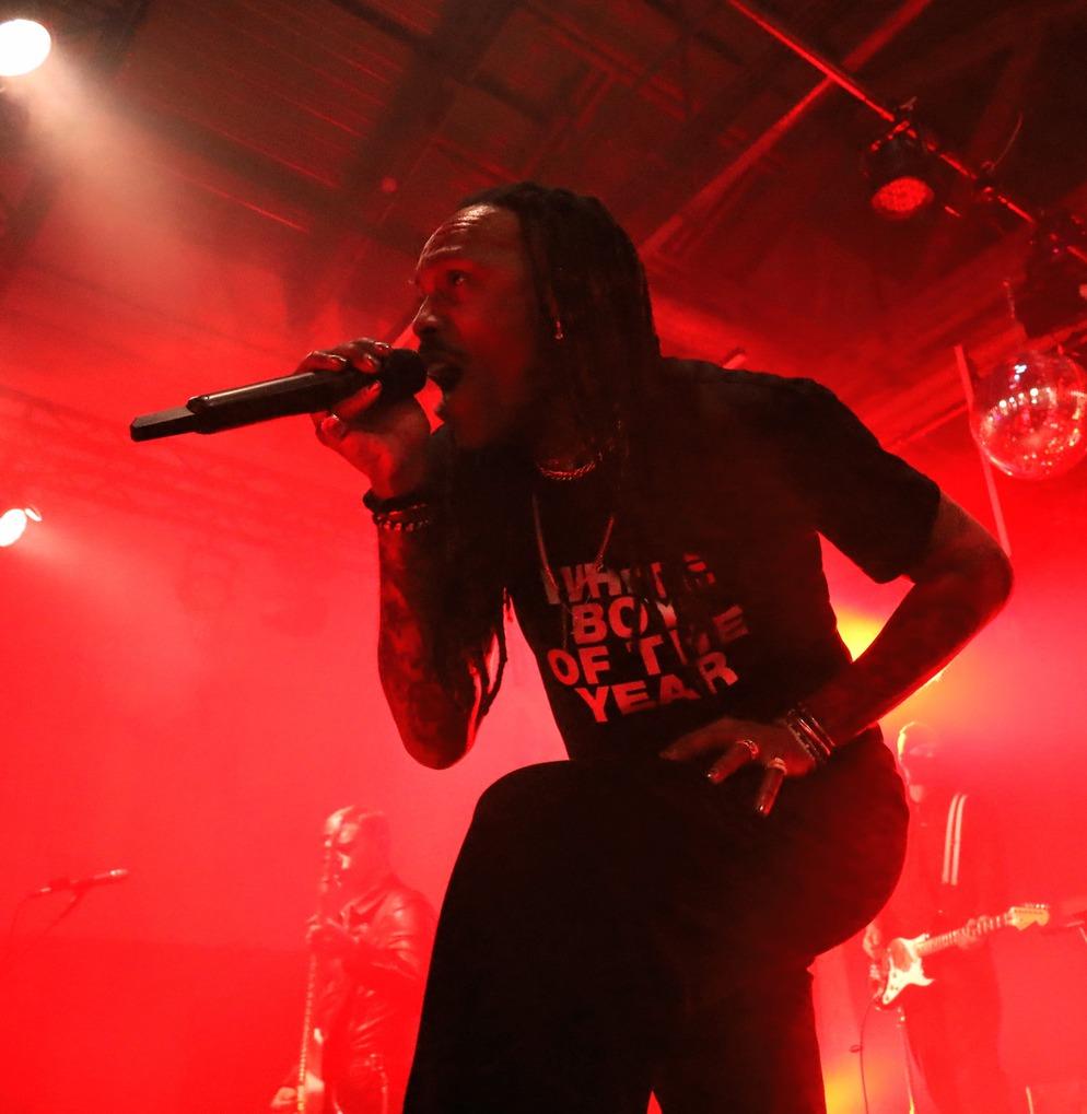 Mat Bastard, chanteur de Skip the Use, chantant avec intensité au micro sur scène, genou à terre, sous des lumières rouges et une boule à facettes.