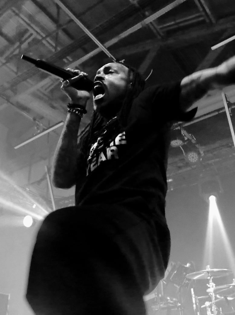 Photographie en noir et blanc intense du chanteur de Skip the Use, hurlant au micro bras levés en concert.