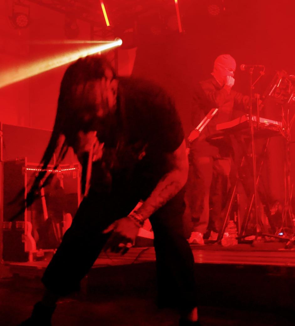 Mat Bastard de Skip the Use en plein mouvement sur scène devant un musicien aux claviers, baignés dans une lumière rouge vive.