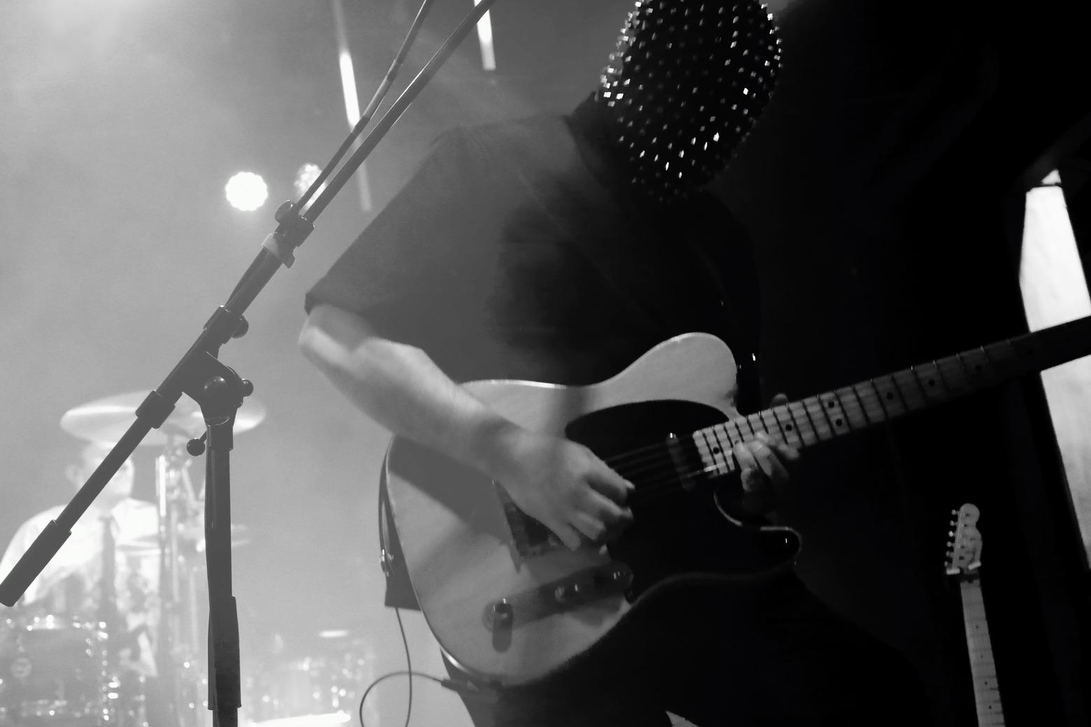 ros plan en noir et blanc du guitariste de Skip the Use jouant de la guitare électrique, le visage couvert par un masque à pointes.