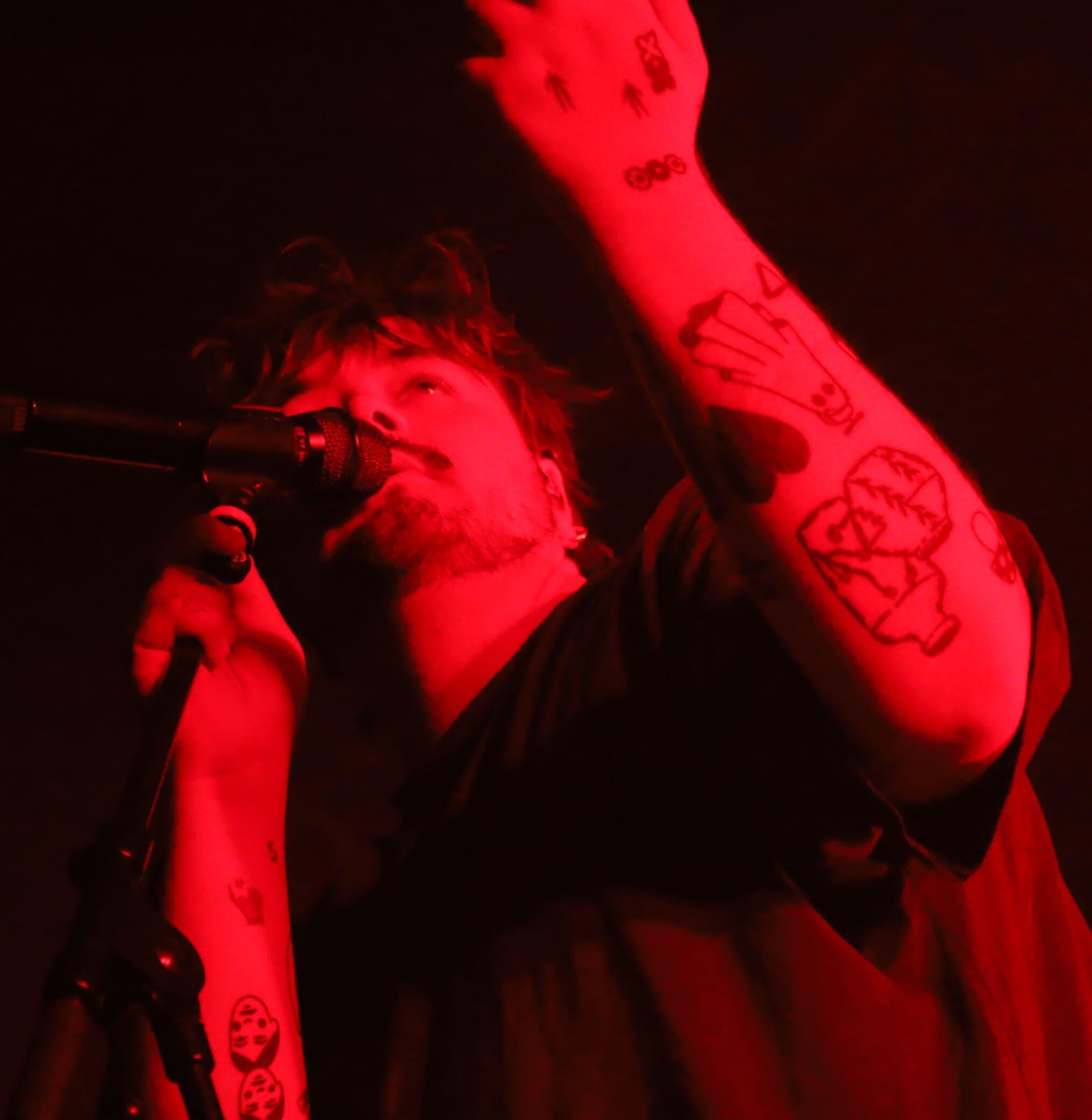 L'artiste Stgraal chantant sur scène sous une lumière rouge intense, un bras levé montrant ses tatouages.