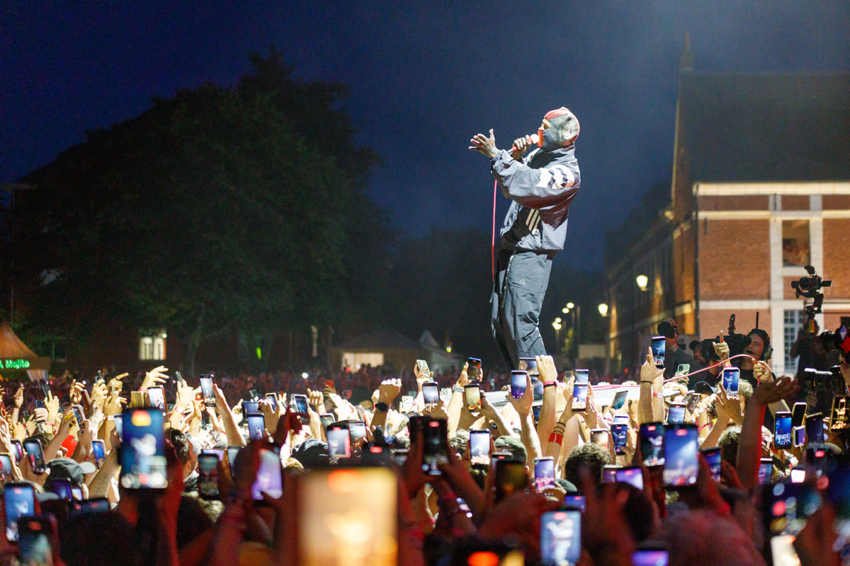 Chanteur de Twenty One Pilots avec cagoule surélevé au-dessus du public qui filme le concert avec des smartphones.