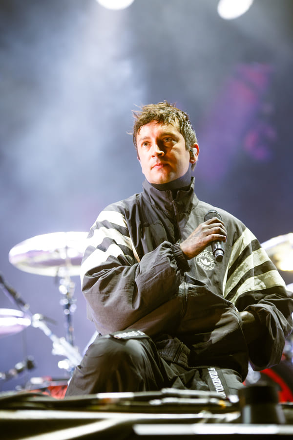Portrait rapproché de Tyler Joseph en veste de sport Adidas tenant un micro sur la scène du Main Square Festival.