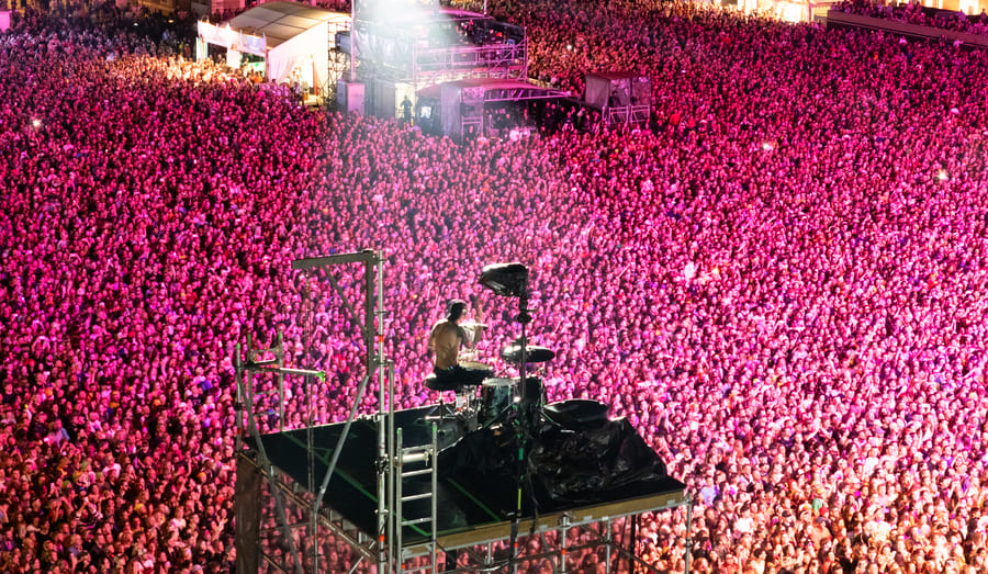 Vue aérienne du batteur Josh Dun de Twenty One Pilots jouant sur une structure surélevée au milieu d'une foule immense.