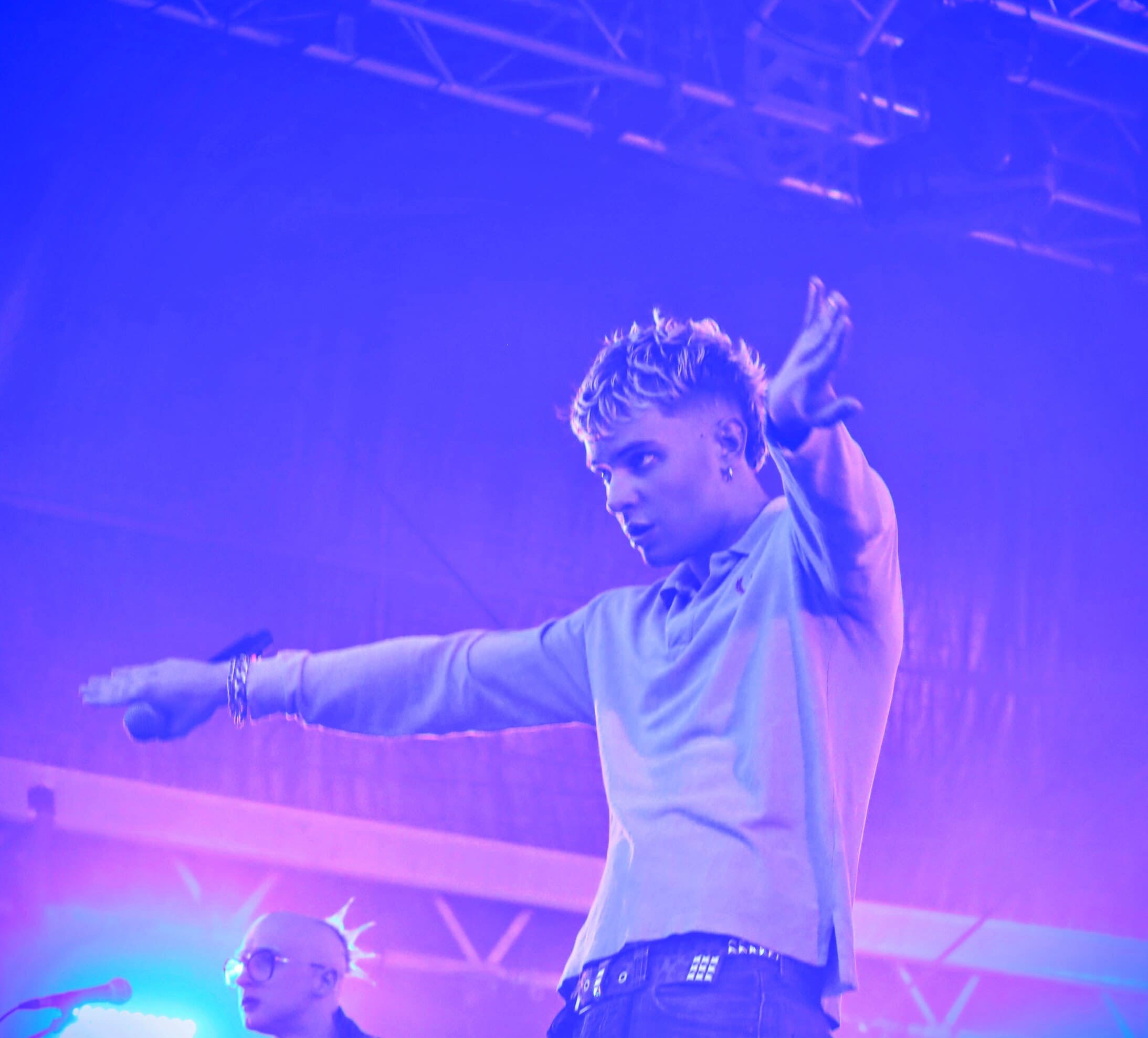 Le chanteur de MDNS tend les bras vers le public lors d'un concert, sous un éclairage violet et bleu avec fumée de scène.