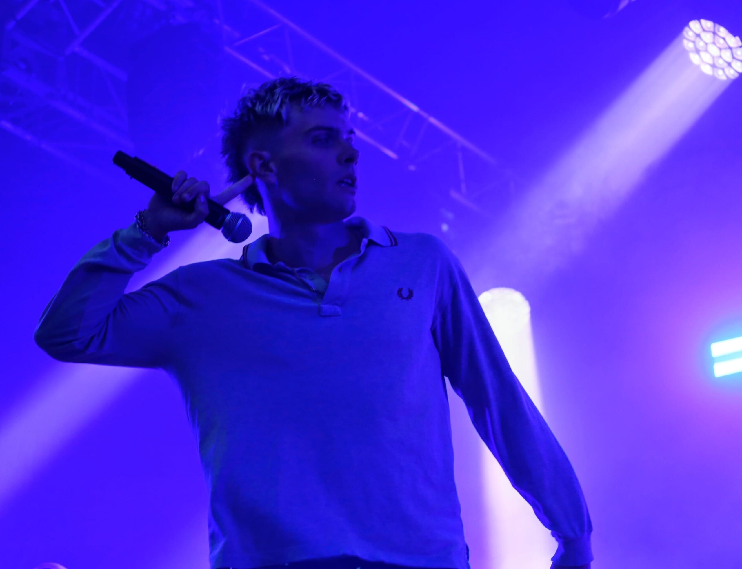 Le chanteur de MDNS encourage le public pendant un concert, micro à la main, sous des lumières violettes et des effets de scène.