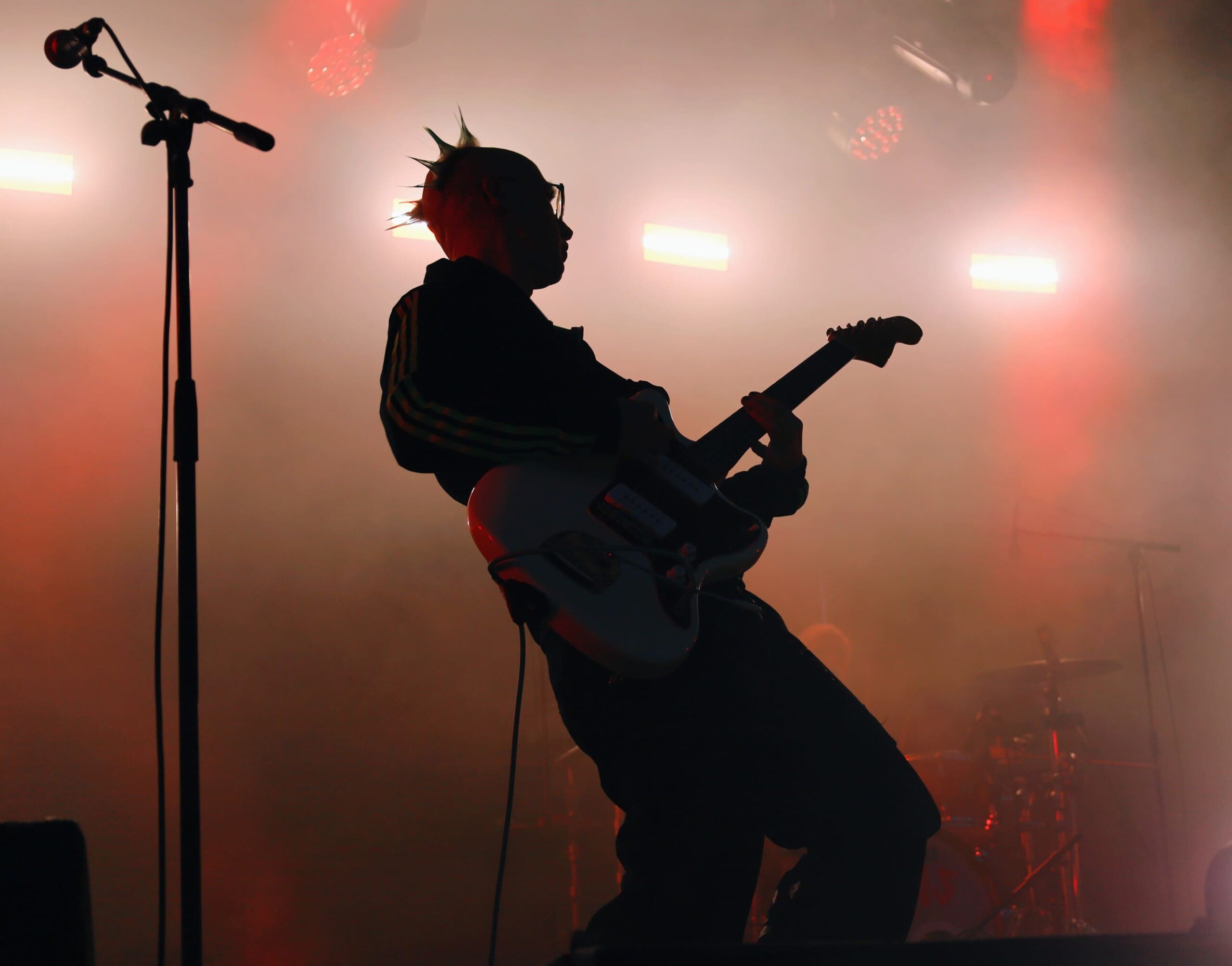 Guitariste du groupe MDNS jouant en silhouette sur scène, éclairé par des projecteurs rouges et une atmosphère enfumée.