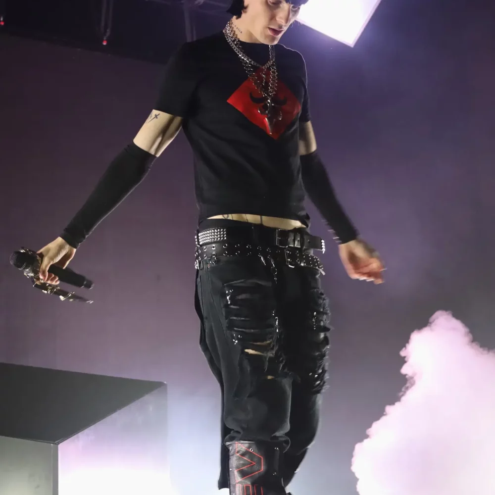 Artiste sur scène tenant un micro, éclairé par une lumière blanche avec de la fumée derrière lui.