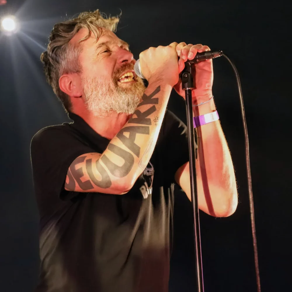 Le chanteur des Fatals Picards sur scène lors d’un concert éclairé par un spot lumineux blanc.